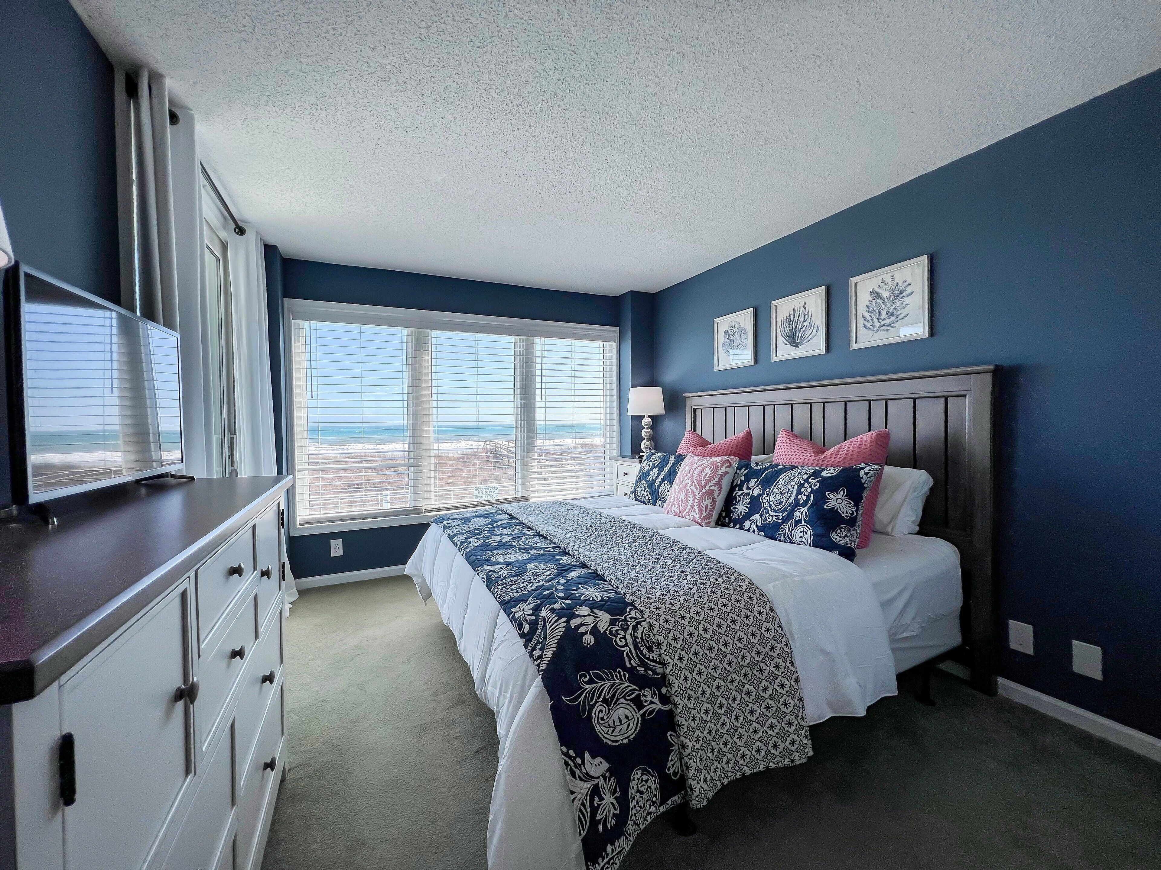 Ein Schlafzimmer mit einem großen Bett, einer Kommode und einem Fenster mit Blick auf den Strand.