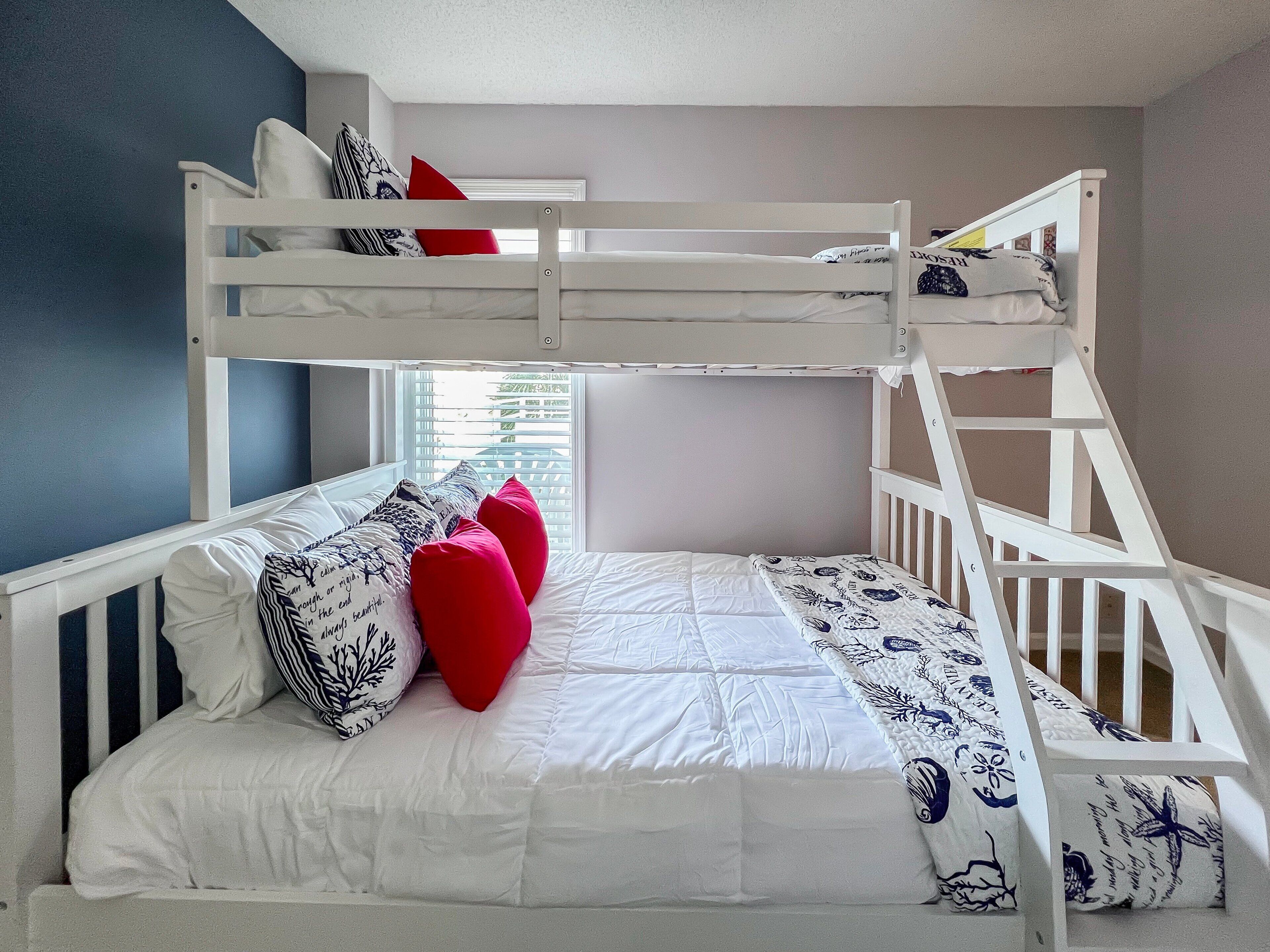 Un lit superposé avec des barreaux et du linge de lit blancs, doté d’une fenêtre avec des stores et offrant une vue sur la verdure à l’extérieur.