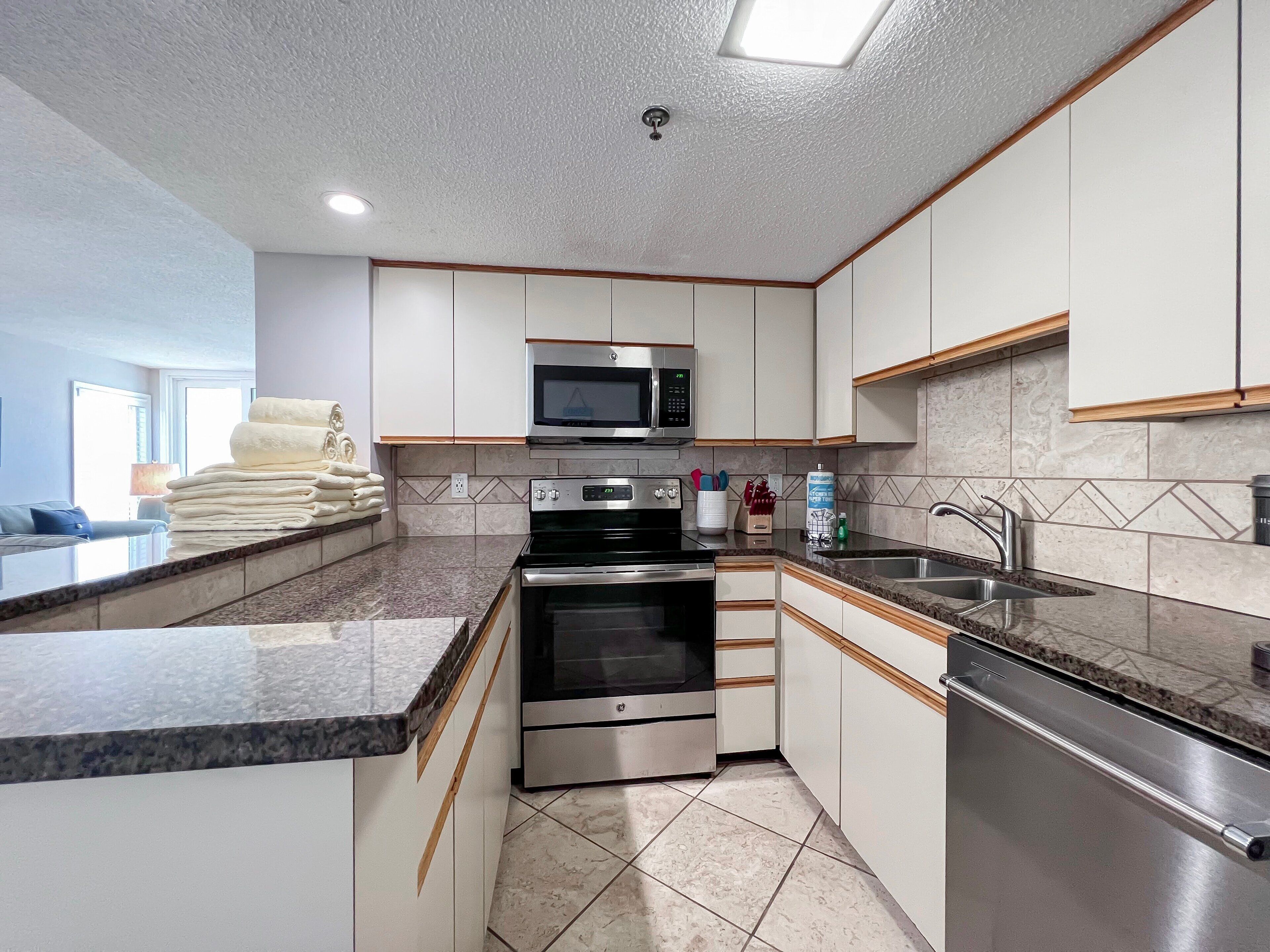 A modern kitchen with white cabinets, stainless steel appliances, a microwave, oven, and a sink.