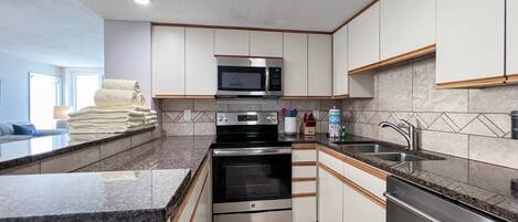 A modern kitchen with white cabinets, stainless steel appliances, a microwave, oven, and a sink.