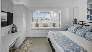 Ein Schlafzimmer mit einem großen Bett, einer Sitzbank mit Kissen, einem Fernseher und Blick auf die Stadt.