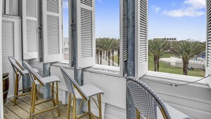 Ein Balkon mit Korbstühlen, weißen Fensterläden und Blick auf Palmen und Gebäude.