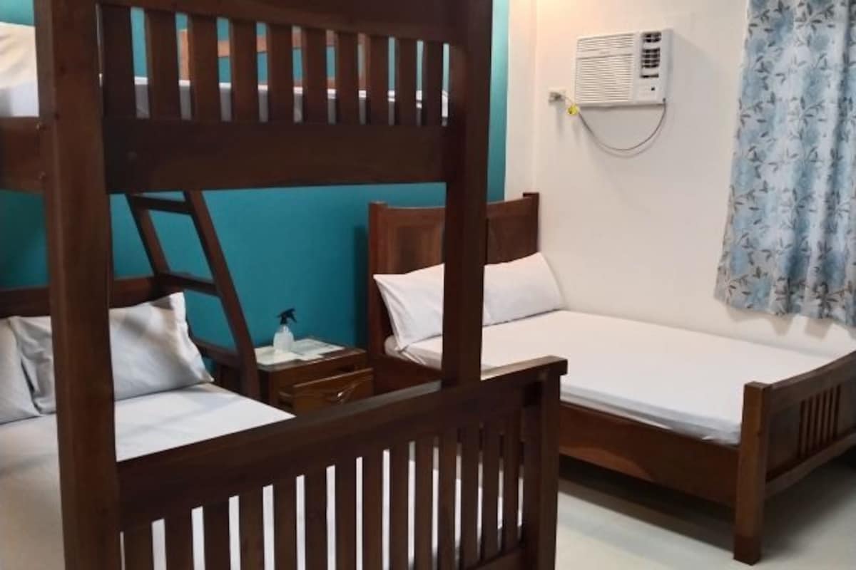 Ein Zimmer mit Etagenbetten, einem Nachttisch mit Lampe, einer Wand-Klimaanlage und einem Vorhang.