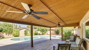 Eine überdachte Terrasse mit Pool, Gartenmöbeln und Deckenventilatoren.