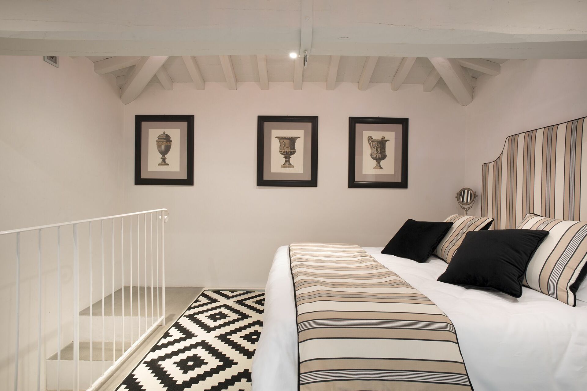 Un dormitorio con cama, almohadas, un cabecero a rayas y tres cuadros en la pared.