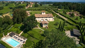 A large villa with a swimming pool, surrounded by lush gardens and a hilly landscape.