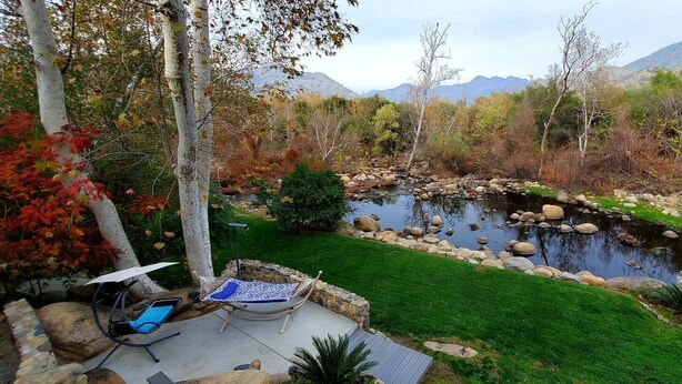 A patio with a hammock and a chair, a small pond, and a view of mountains. - Peaceful Riverfront Resort #2 (Three Rivers)