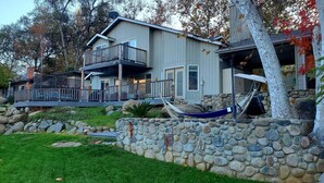 A two-story house with a stone retaining wall, a balcony, and a hammock. - Peaceful Riverfront Resort #2 (Three Rivers)
