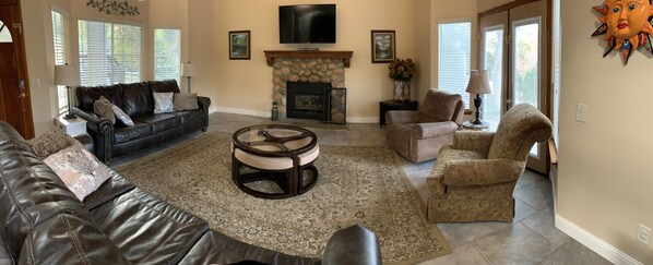 A living room with a stone fireplace, leather sofas, a coffee table, and a television mounted above the fireplace. - Peaceful Riverfront Resort #2 (Three Rivers)