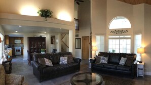 A spacious living room with two black leather sofas, a glass coffee table, and a dining area with a kitchen in the background. - Peaceful Riverfront Resort #2 (Three Rivers)