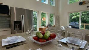 Un comedor con una mesa lista para cuatro personas, un frutero y una cocina al fondo.