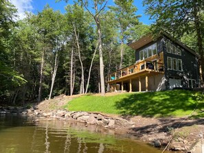A cabin with a deck overlooking a river, surrounded by trees. - Secluded lakefront home With an EV charger (Monticello)