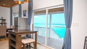 A room with a wooden table and chairs, a refrigerator, and a view of the ocean through a sliding glass door. - Ultimate Vacation in Paradise at BLU (Rolletown)