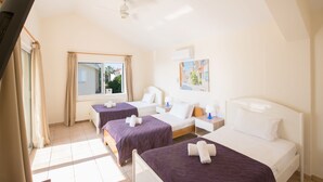A hotel room with two beds, a ceiling fan, a window with curtains, and a painting on the wall. - Ayia Napa Holiday Villa At26 (Sotira)