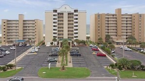 Ein Hotel mit einem zentralen Gebäude, das 'Tropical Winds' heißt, und mehreren umgebenden Gebäuden. Ein Parkplatz mit mehreren Autos ist vorhanden.
