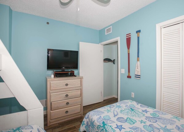 A bedroom with a TV on a dresser, a bed with a starfish-patterned bedspread, and a door with a fish decoration.