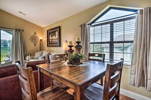 A dining area with a wooden table and chairs, a sofa, a lamp, and a window with blinds. - Stroll to Branson Strip: Condo on Golf Course (Branson)