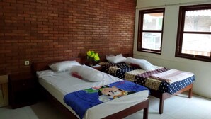 Een kamer met een bakstenen muur, twee bedden met verschillende beddengoed, een klein tafeltje met een bloemenvaas, en een raam met uitzicht op buiten.