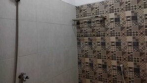 Een douche met een handdouche en een kraan die aan de muur bevestigd is. De douche heeft een betegelde wand met een geometrisch patroon.