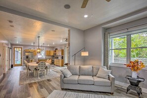Una sala moderna con un sofá gris, una mesa de comedor con sillas, y una cocina al fondo.