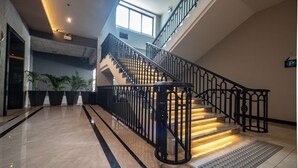 A modern hotel lobby with a marble floor, a staircase with black railings, and potted plants. - Lewit Hotel Pattaya, a member of Radisson Individuals (Pattaya)