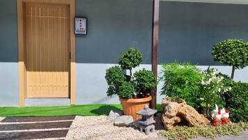 Una entrada tradicional al estilo japonés, con puerta de madera, un pequeño santuario y abundante vegetación cuidada.