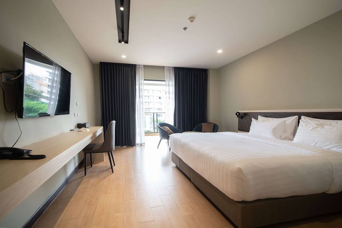 A hotel room with a bed, a desk, a chair, a TV, and a window with curtains.