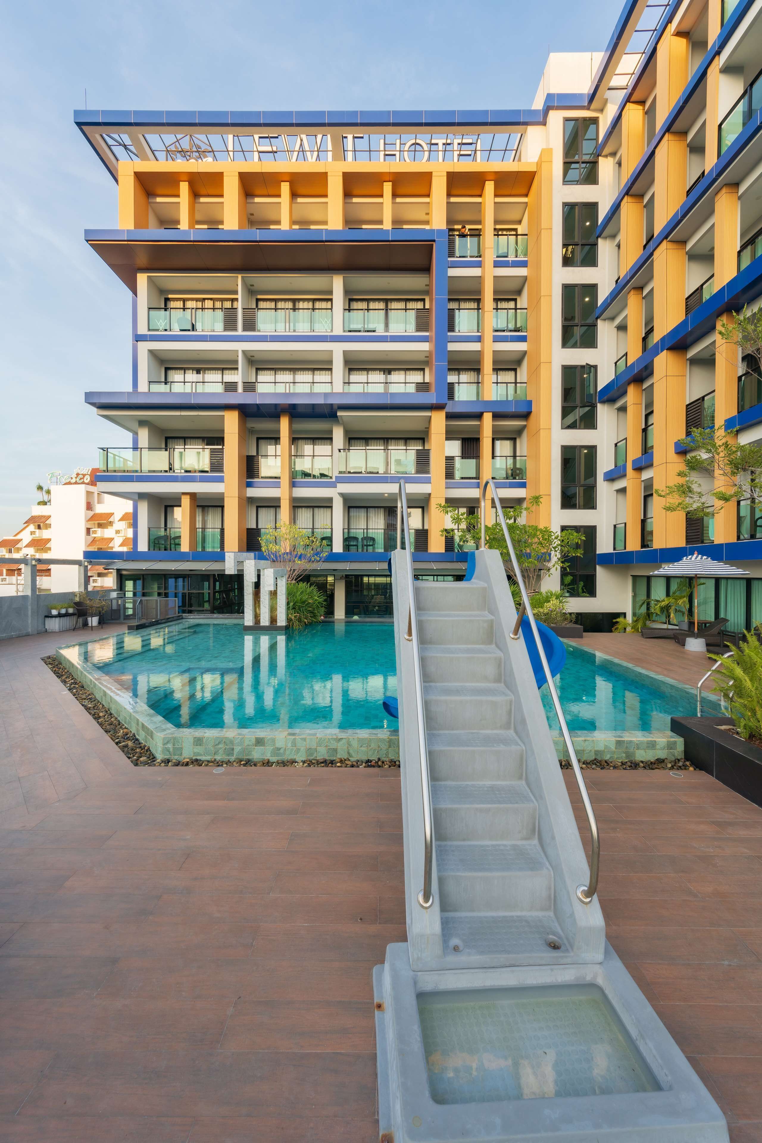 A hotel with a pool, a staircase leading to the pool, and a clear sky.