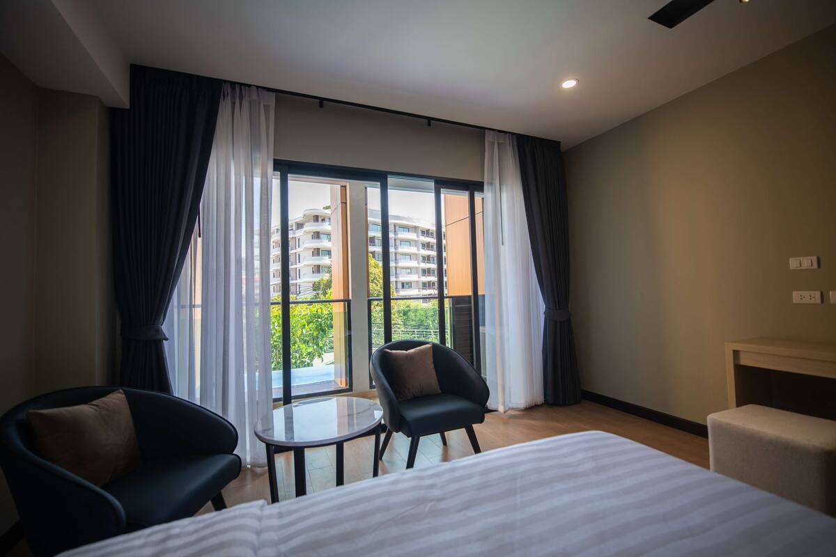 A hotel room with a bed, two armchairs, a small table, and a large window with curtains.