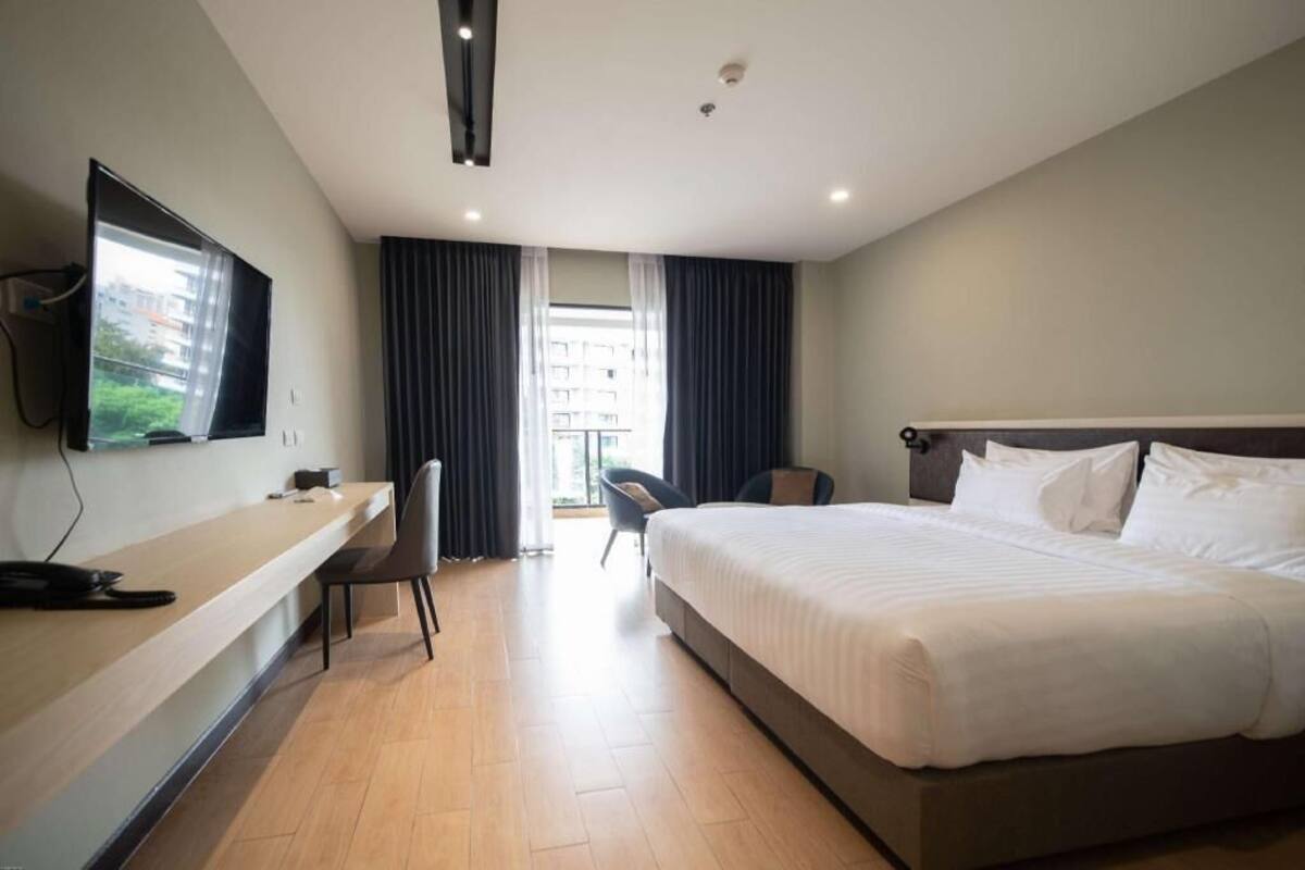 A hotel room with a bed, a desk, a chair, a TV, and a window with curtains.