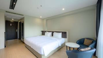 A hotel room with a large bed, a small round table, a blue chair, and a door leading to another room.