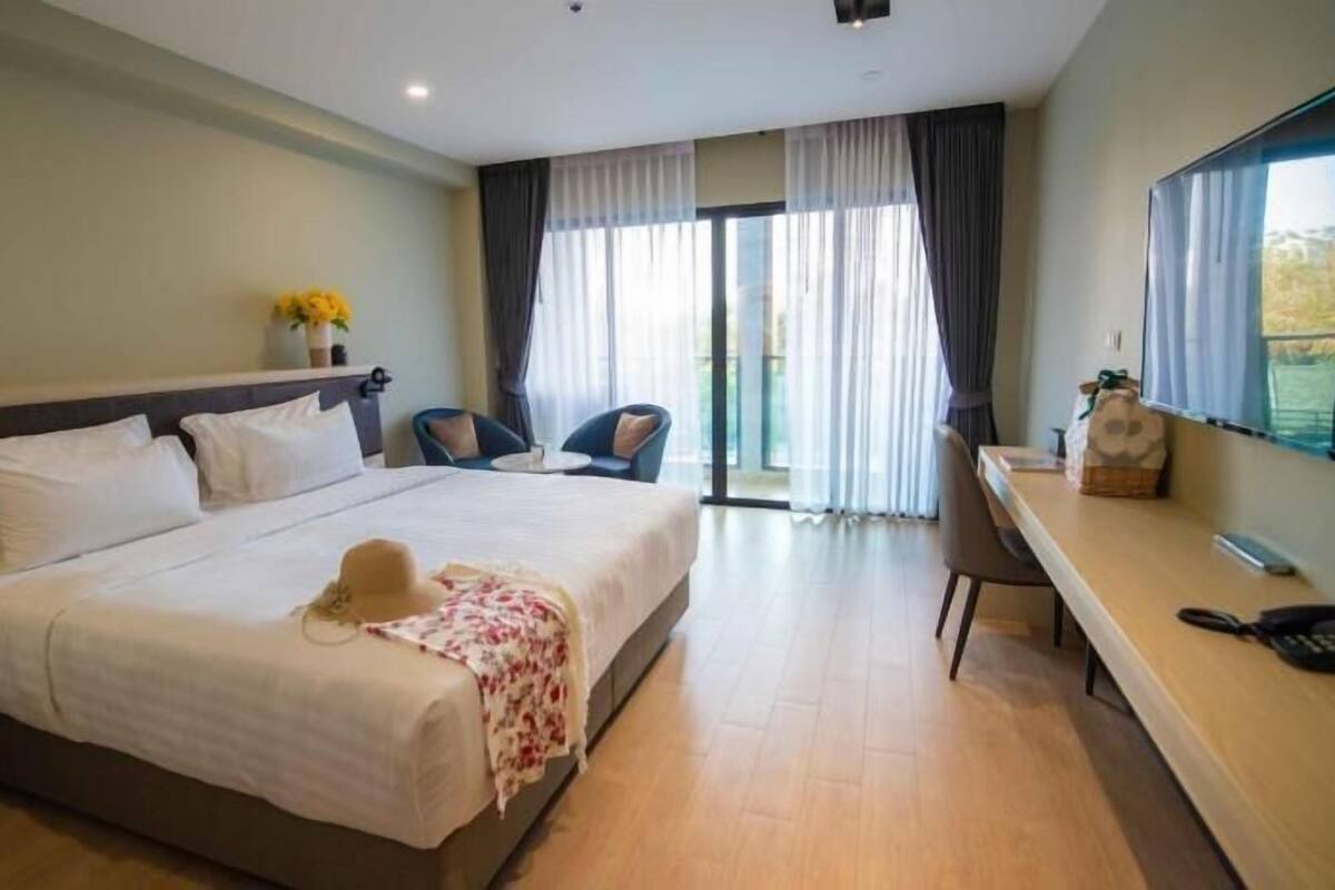A hotel room with a bed, a desk, a chair, and a large window.