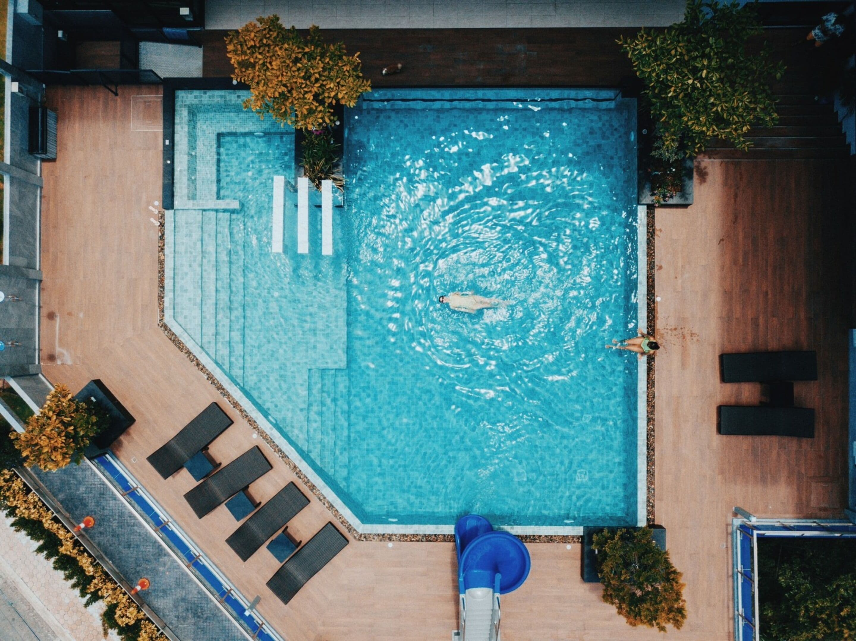 Vista aérea de una piscina rectangular con hidromasaje, rodeada de sillas de descanso y plantas en macetas.