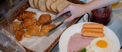 Un bufé de desayuno con pan, cruasanes, salchichas, jamón, huevos y guisantes.