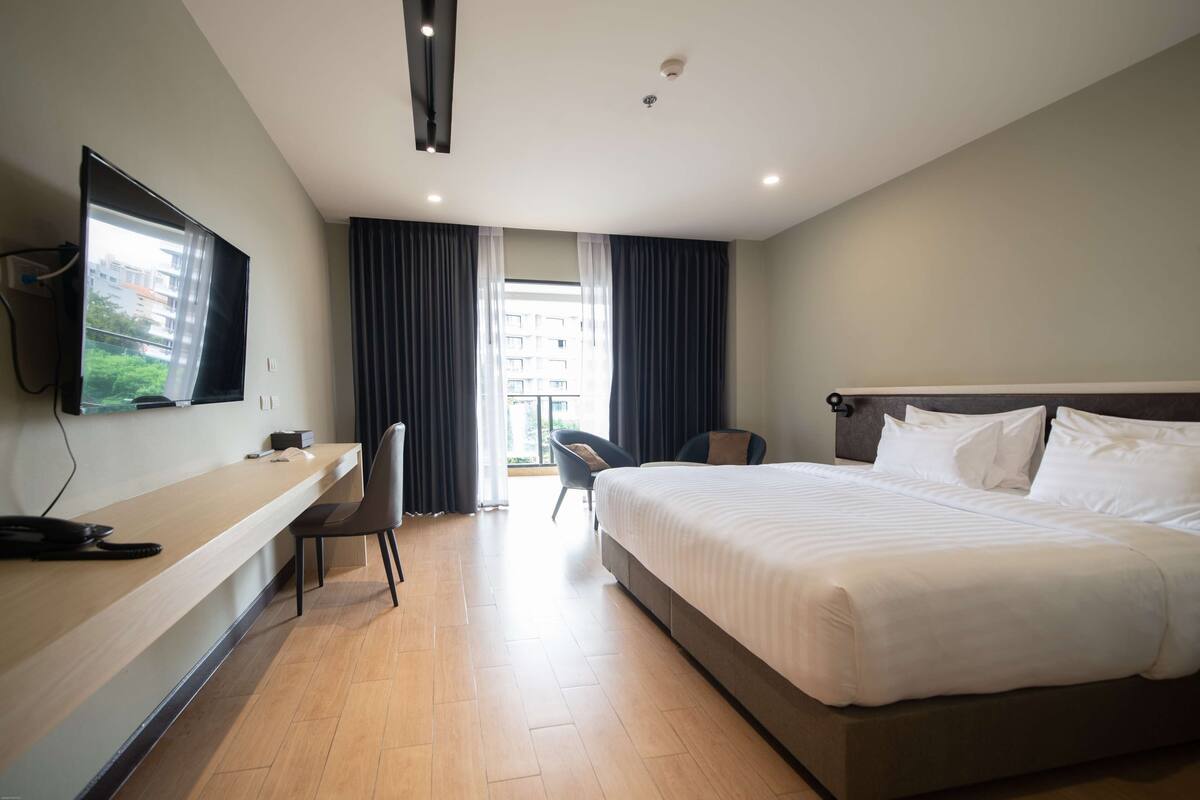A hotel room with a large bed, a desk with a computer, a chair, and a TV on the wall.