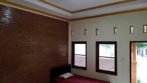 A bedroom with a single bed, a brick wall, and two windows.