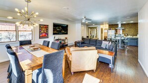 A spacious living area with a wooden dining table, comfortable seating, a kitchen in the background, and a ceiling fan. - Steps to Main St! Red River Condo w/ Mtn-View Deck (Red River)