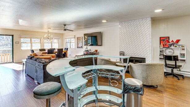 A modern living room with a curved glass table, a sofa, and a TV mounted on the wall. - Steps to Main St! Red River Condo w/ Mtn-View Deck (Red River)