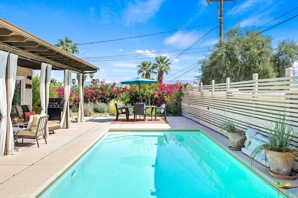 Une piscine agrémentée d’une pergola, d’un espace salon extérieur et de plantes en pot.