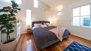 Ein Schlafzimmer mit Bett, Nachttischen, einer Zimmerpflanze und einem Fenster.