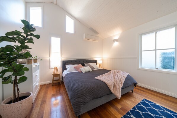 A bedroom with a bed, bedside tables, a potted plant, and a window.