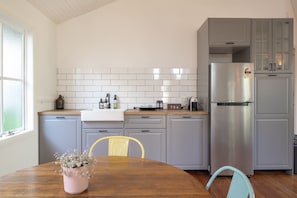 A modern kitchen with grey cabinets, a stainless steel refrigerator, and a wooden dining table with chairs.