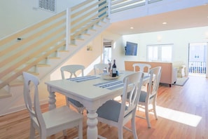 Un salon moderne avec un escalier blanc, un coin repas avec une table et des chaises, et un canapé.