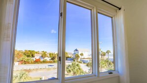 Una stanza con una grande finestra che offre vista su una zona residenziale con case, palme e una spiaggia.