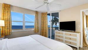 Una habitación de hotel con una cama grande, un televisor en un tocador y un balcón con vista al océano.