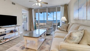 Una sala de estar con televisor, una mesa de centro de vidrio, sofá y balcón con vistas a la playa.