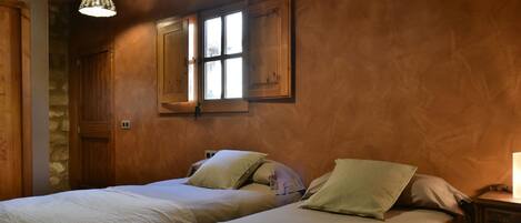 A room with two beds, wooden walls, a stone wall, and a window with shutters.
