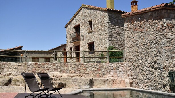 Un bâtiment en pierre avec une piscine et des chaises longues.