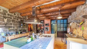 Une cuisine rustique dotée d’un grand îlot central, de murs en pierre, de poutres en bois et d’appareils électroménagers modernes.