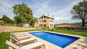Eine Steinvilla mit Swimmingpool, Liegestühlen und einer Steinsäule.